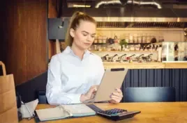Millennial small business owner calculating finance bills of activity. Female entrepreneur using digital tablet to pay invoice and taxes and to calculate financial expenses of new bar restaurant