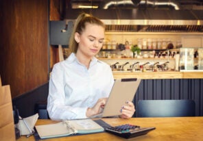 Millennial small business owner calculating finance bills of activity. Female entrepreneur using digital tablet to pay invoice and taxes and to calculate financial expenses of new bar restaurant