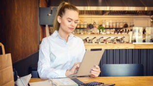 Millennial small business owner calculating finance bills of activity. Female entrepreneur using digital tablet to pay invoice and taxes and to calculate financial expenses of new bar restaurant