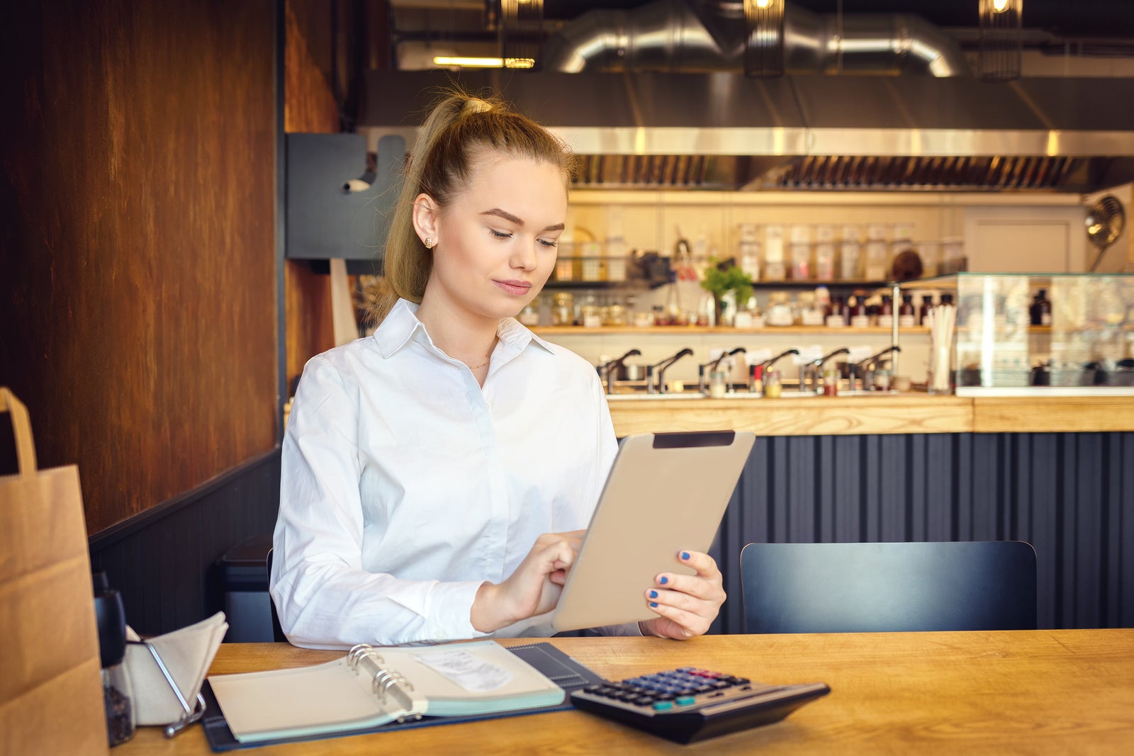 Millennial small business owner calculating finance bills of activity. Female entrepreneur using digital tablet to pay invoice and taxes and to calculate financial expenses of new bar restaurant