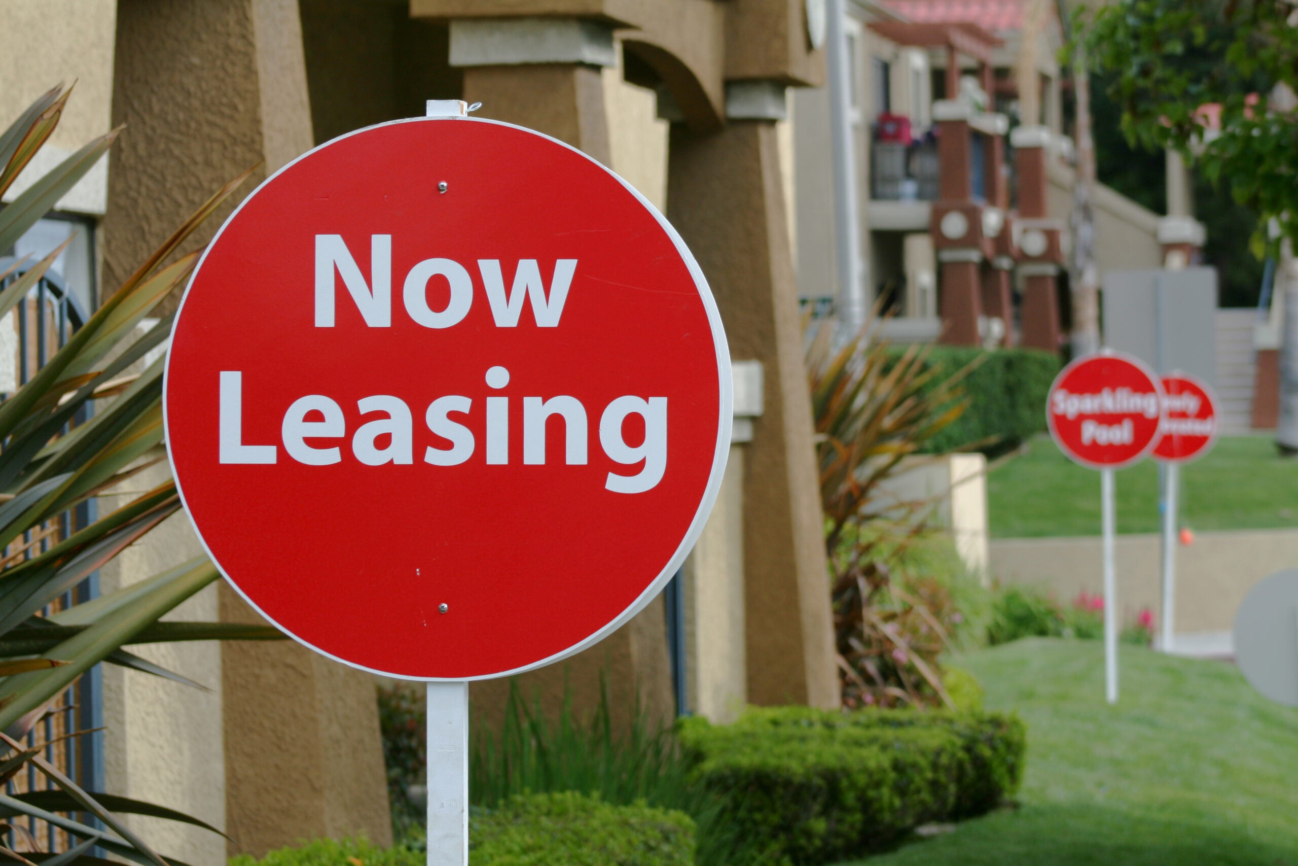 Red and white Now Leasing sign in front of a Rental Property.