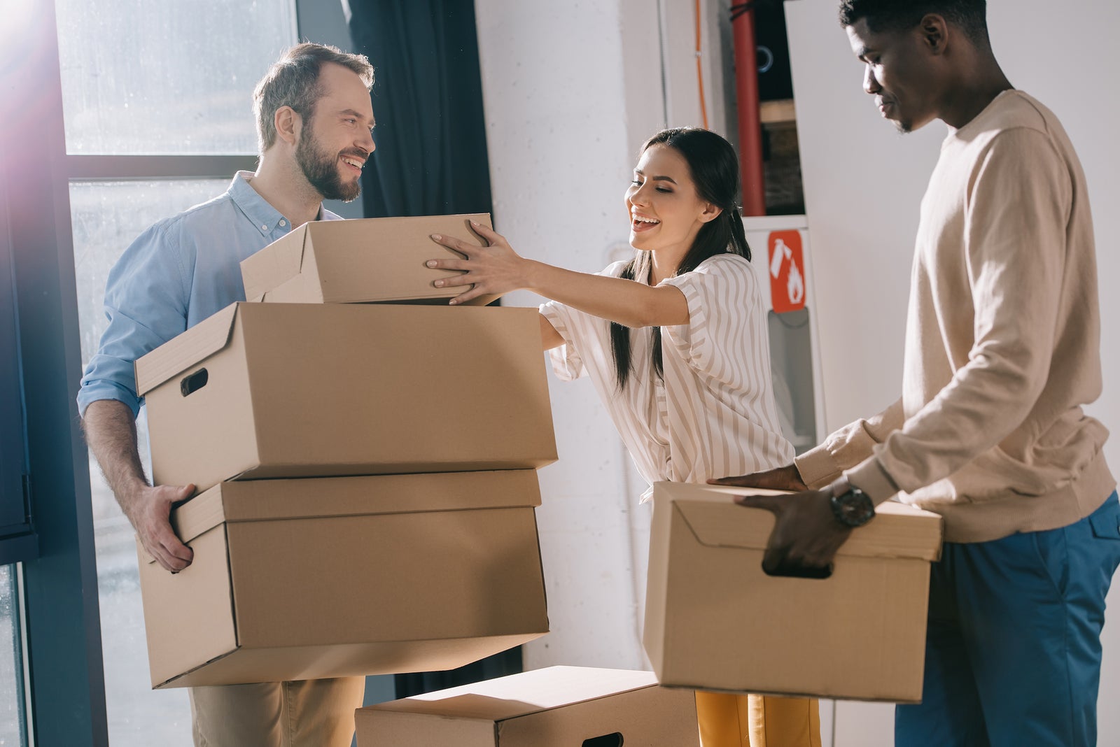 smiling multiethnic coworkers carrying cardboard boxes during relocation in new office