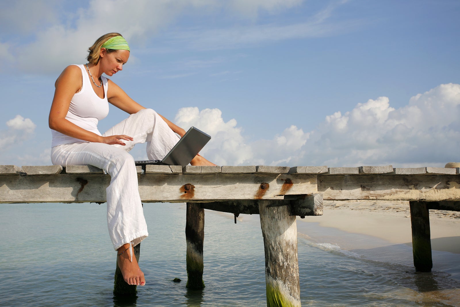 Woman in white looking at a laptop on a tropical boardwalk