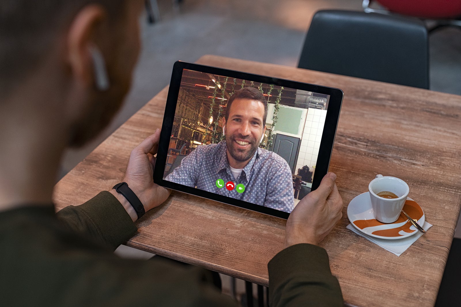 Smiling business partners talking through video call. Back view of man in coffe shop doing video chat calling a friend. Young man and his friend talking to each other through a videocall on tablet.