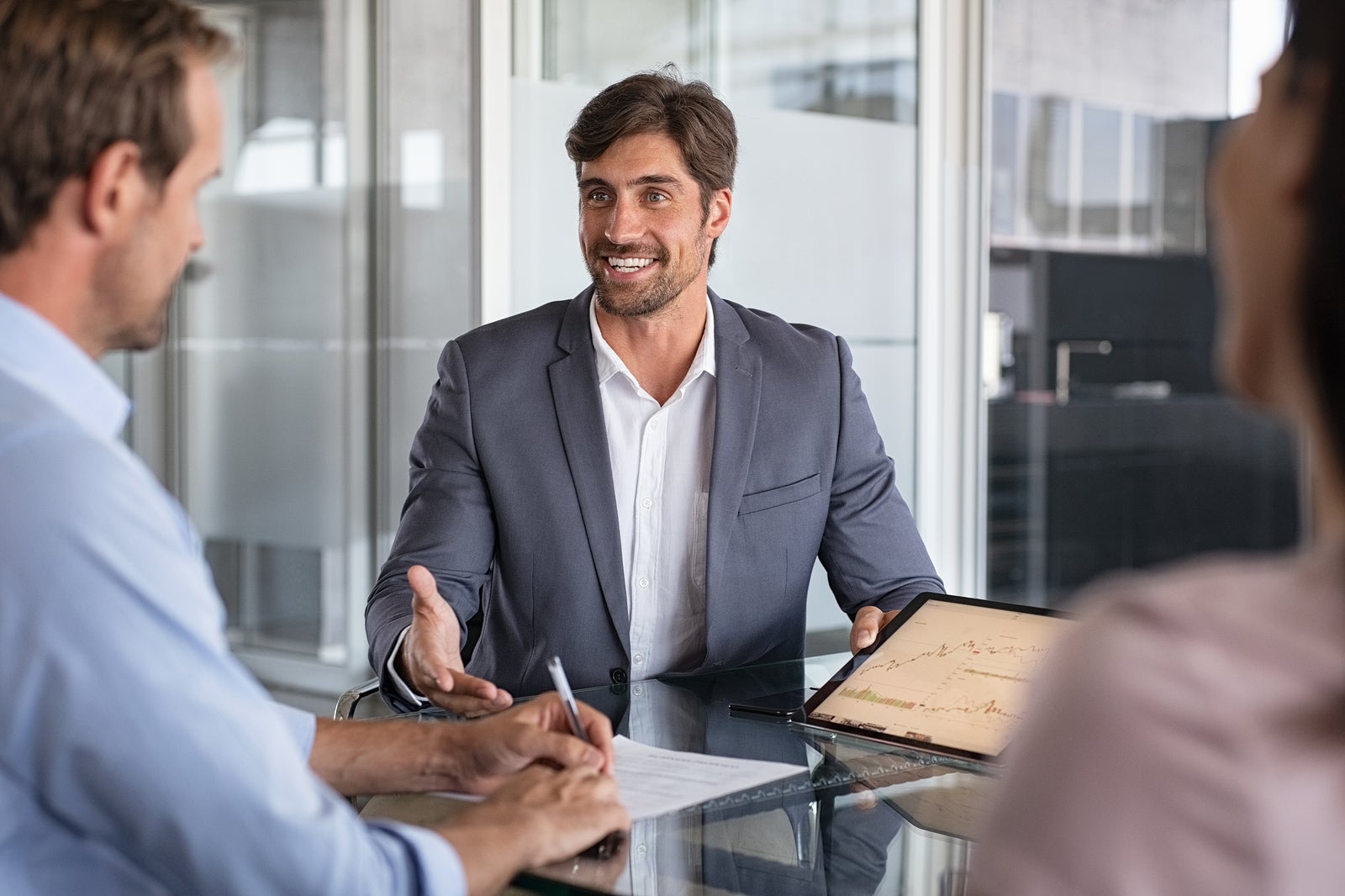 Confident financial agent showing growth graph to couple. Mid couple meeting financial advisor for investment. Business people discussing the charts and graphs showing the results.