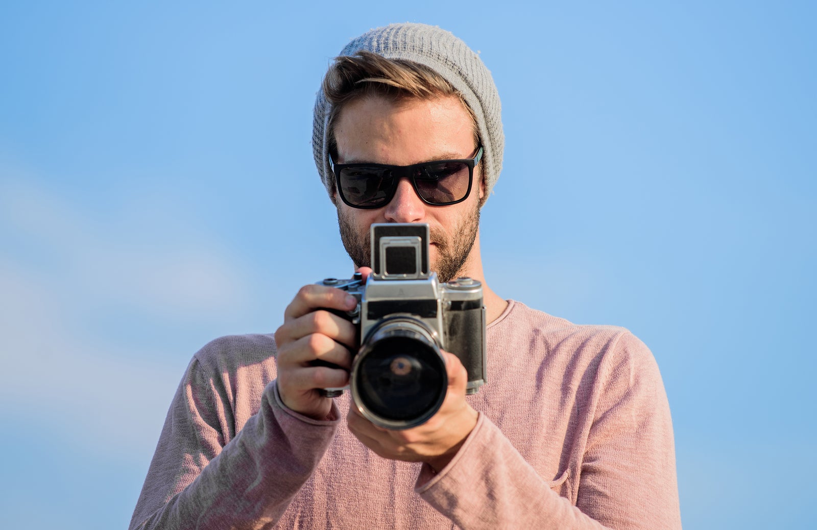 Photojournalist concept. Hipster reporter taking photo. Manual settings. Travel blogger. Professional photographer. Handsome photographer guy retro camera. Guy photographer outdoors sky background