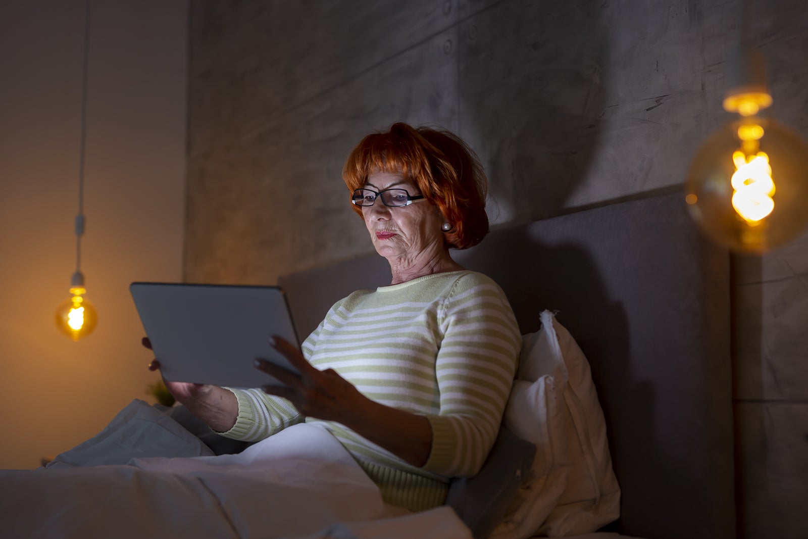 Beautiful senior woman wearing pajamas sitting in bed, reading an ebook on tablet computer