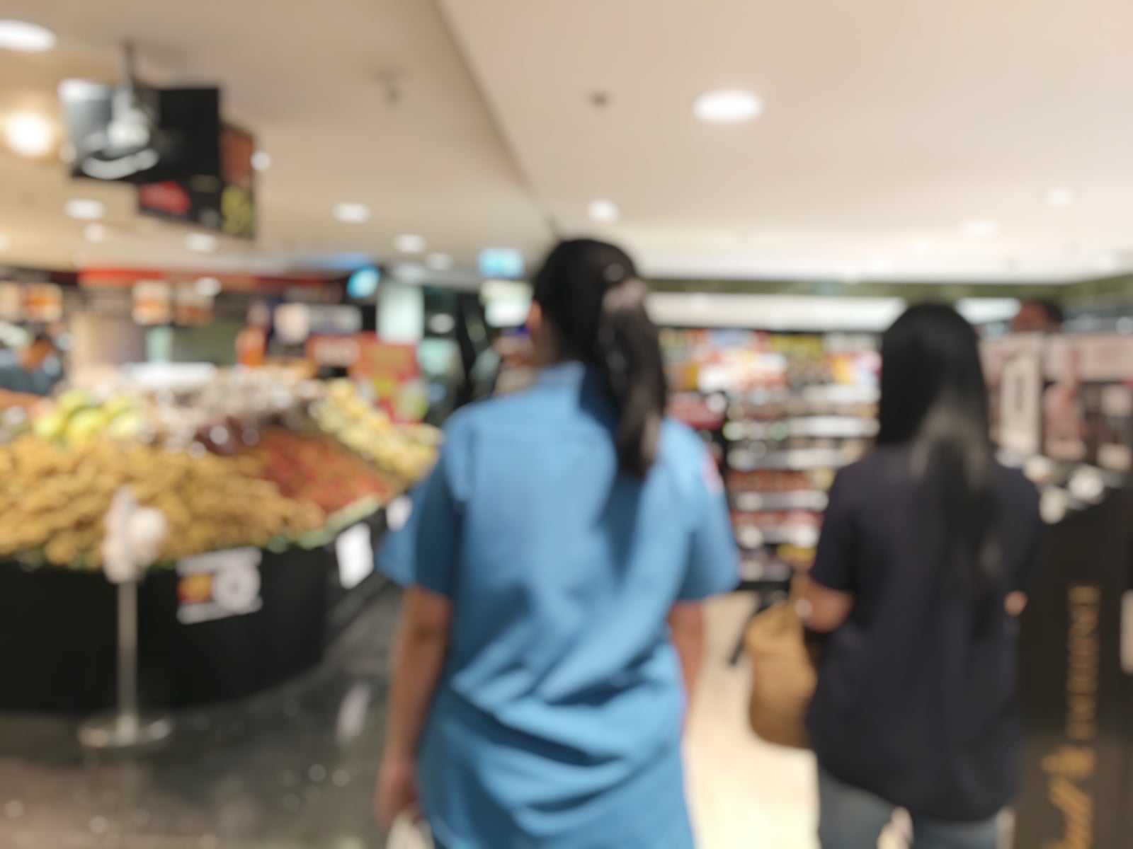 Blurred image of cashier with long line of people at check-out counter of supermarket. Customers paying with credit card or cash to store clerks, full cart of groceries. Cashier register concept