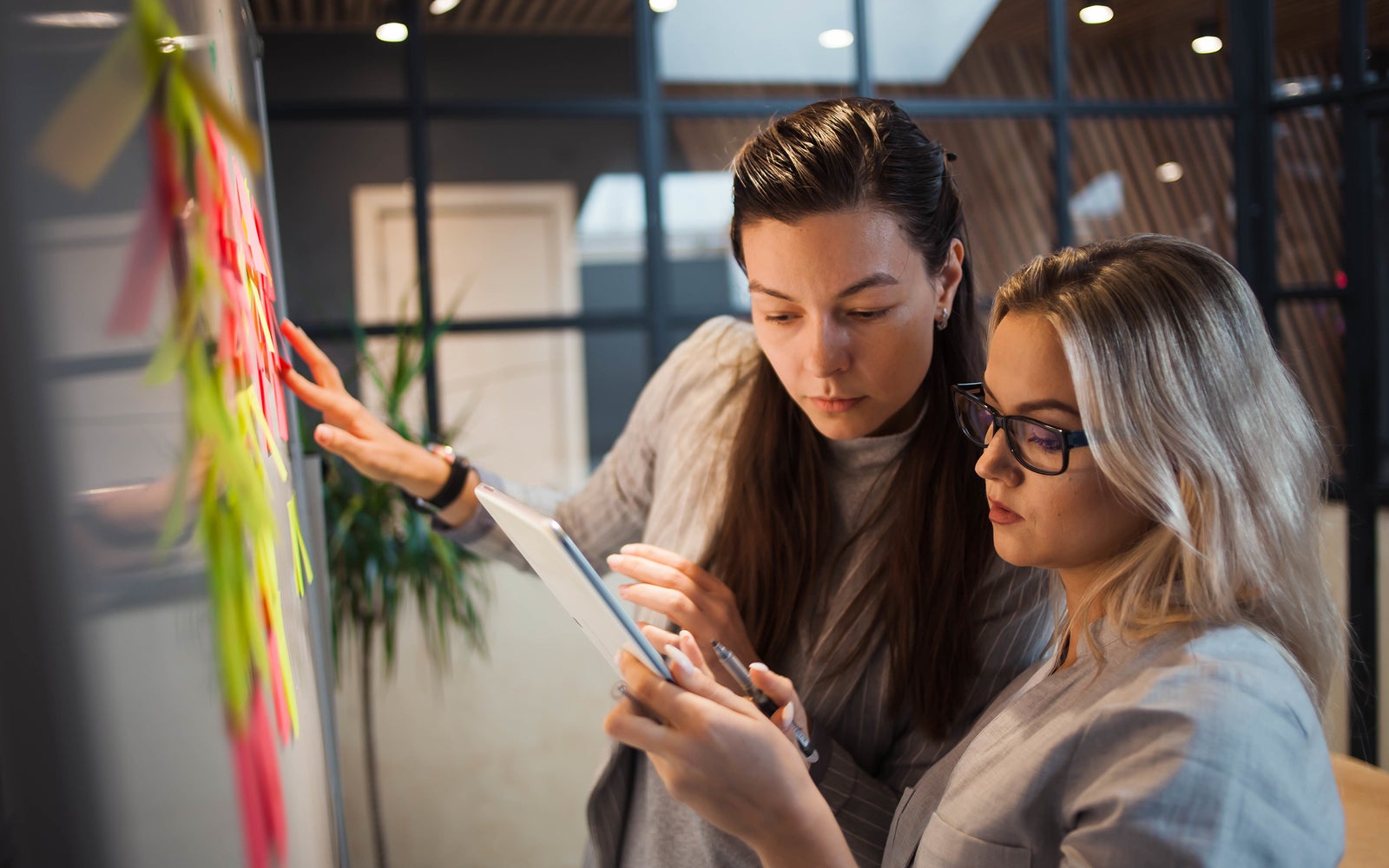 Teamwork, project management, agile methodology. Two young business women in the office are working on a startup. Colleagues plan work and stages of development of company, glue sticky leaves on Board