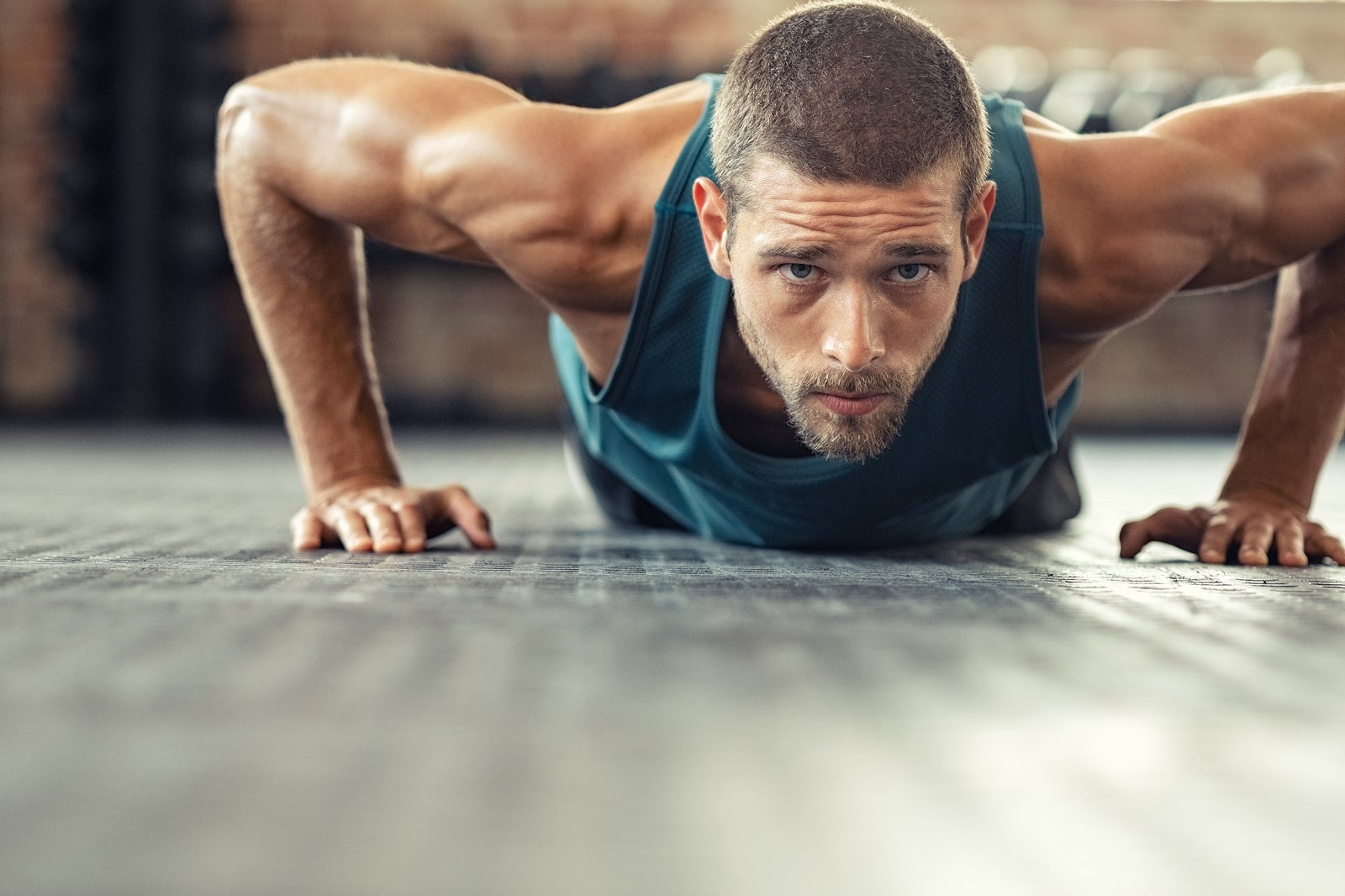 Young athlete doing push ups as part of bodybuilding training. Muscular guy doing a pushup on floor at crossfit gym. Determined athletic guy in sportswear exercising.
