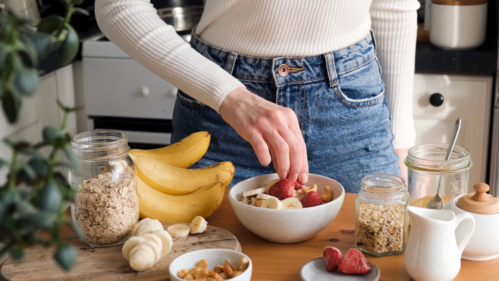 Adding fruits to breakfast oatmeal porridge bowl. Woman preparing healthy breakfast at the kitchen. Concept of healthy eating and lifestyle