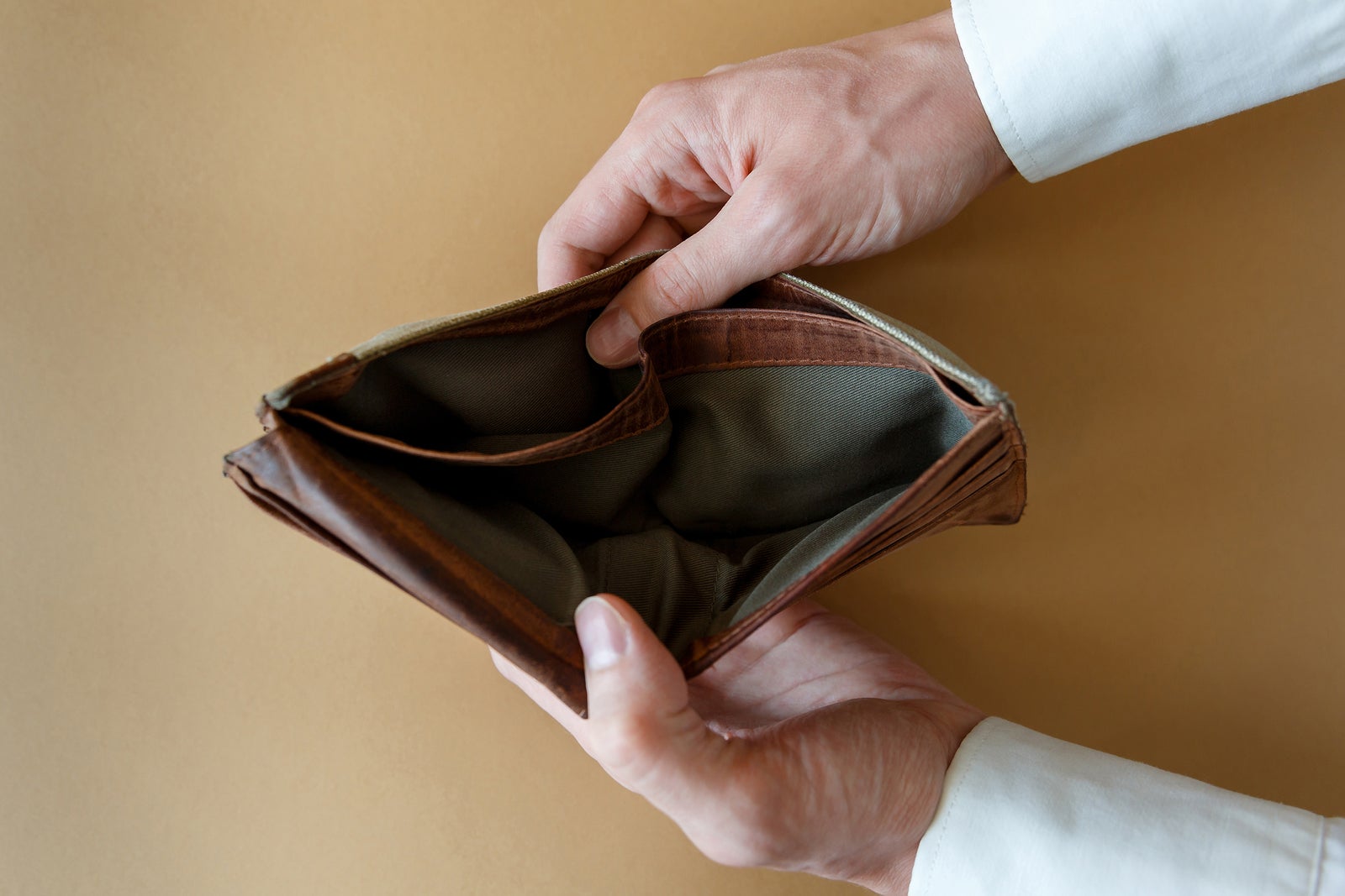 Empty wallet in the hands of a man on a light solid background, top view. Bankruptcy and insolvency in the economy and finance.