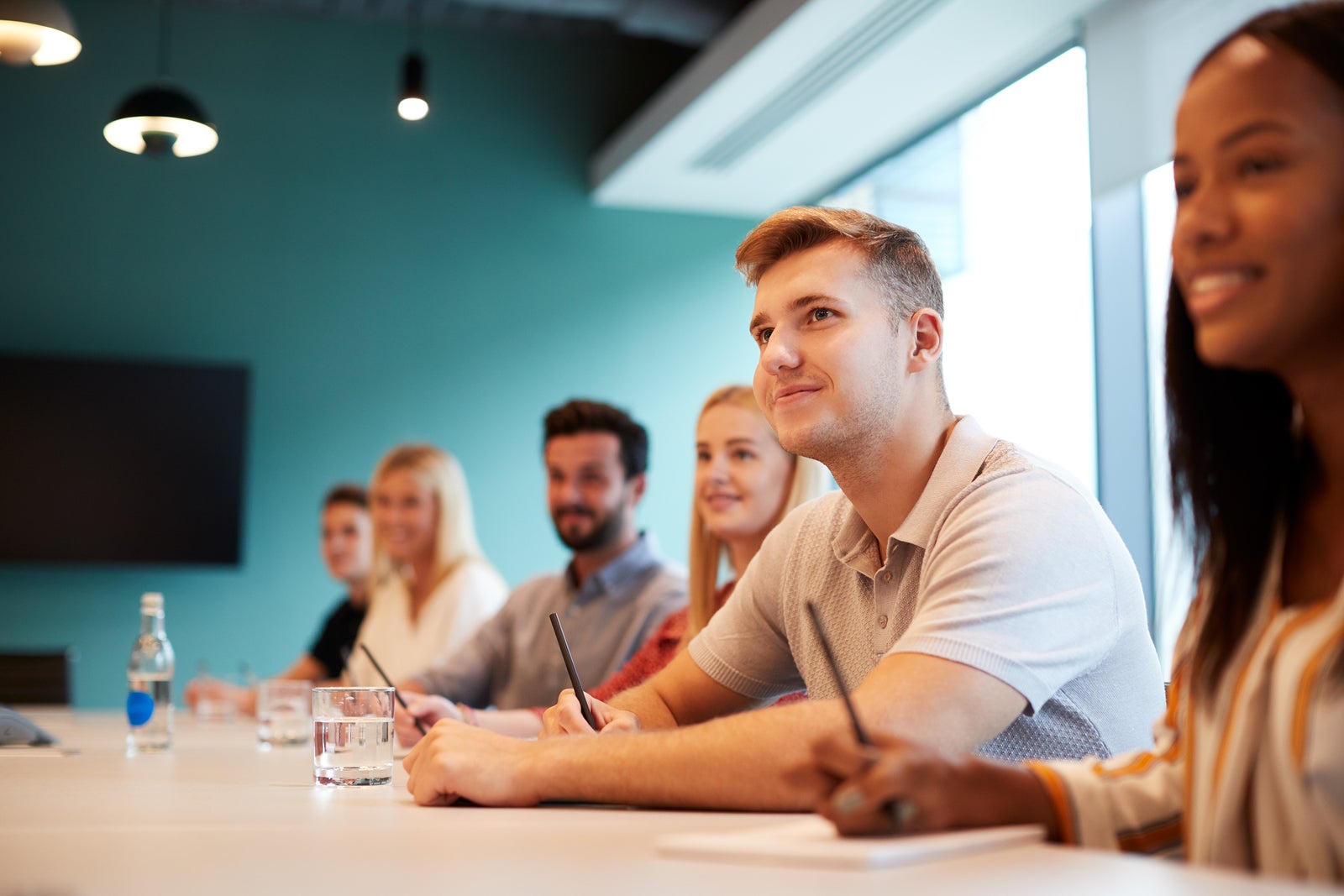 Group Of Young Candidates Sitting At Boardroom Table Listening To Presentation At Business Graduate Recruitment Assessment Day