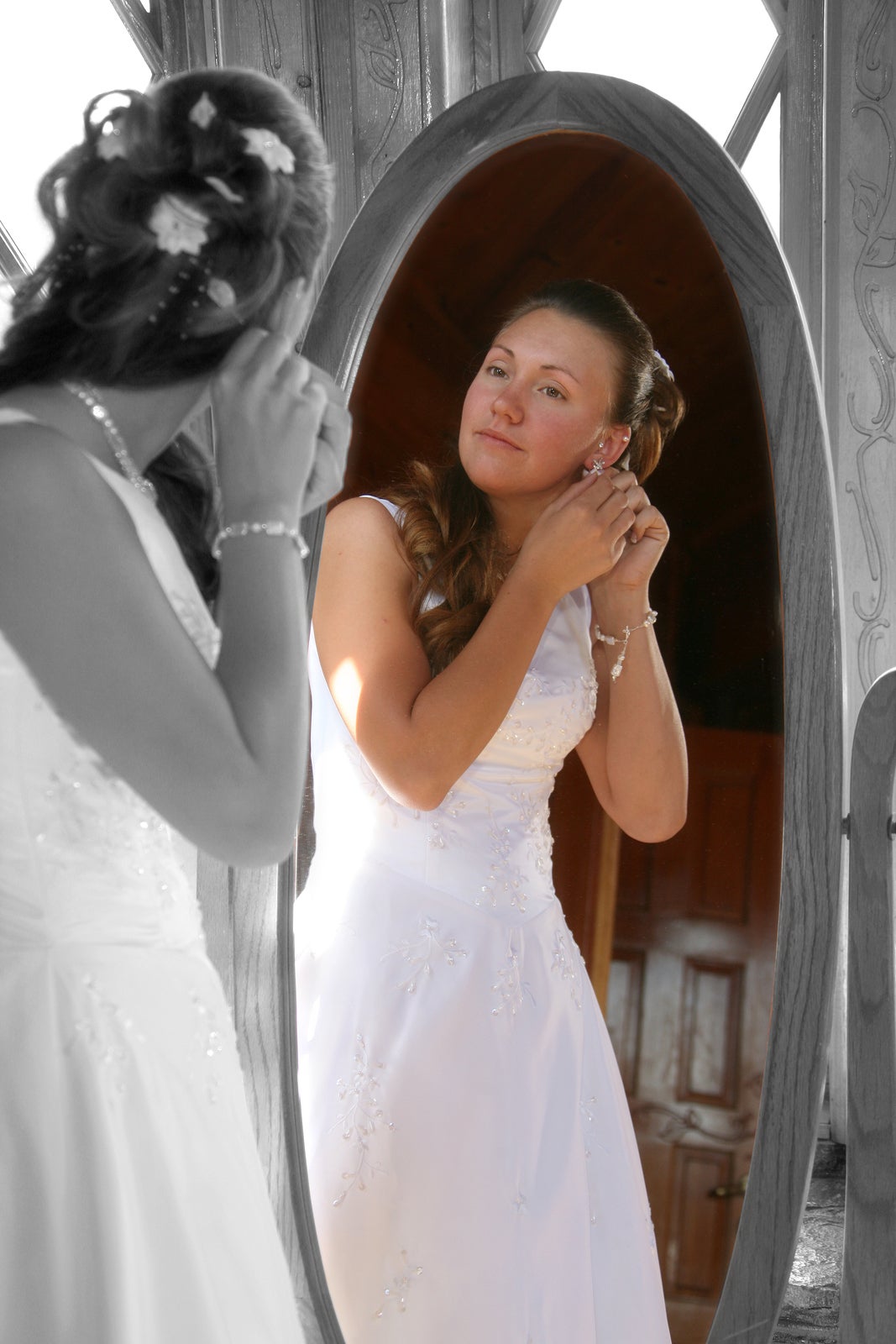 a bride uses a large mirror to put on her jewlery before the wedding