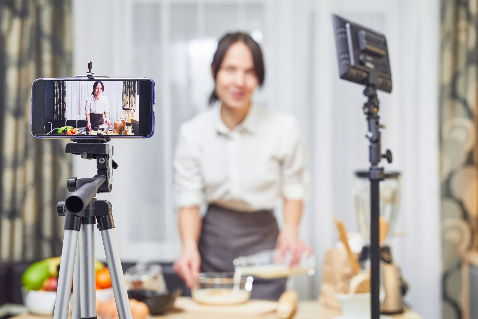 Vlogger freelance job, food concept. Young caucasian woman cooking and recording live video for vlog and social media with phone camera in their kitchen