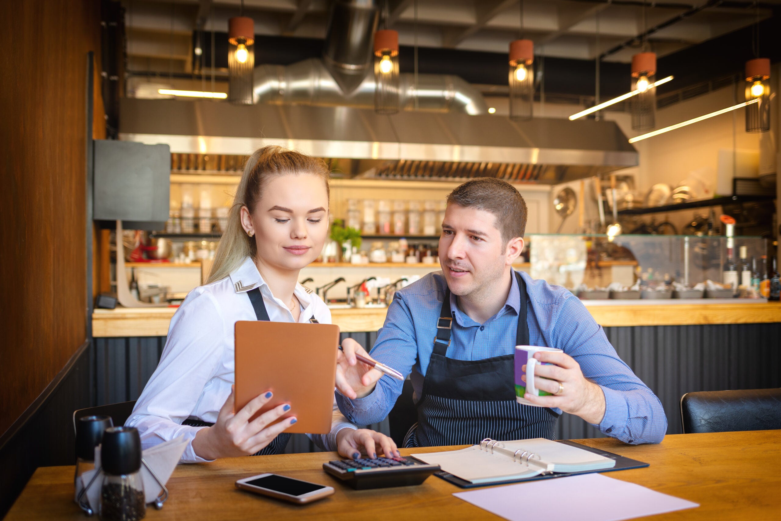 Young man and woman going through paperwork together in their restaurant. Small family restaurant owners discussing finance calculating bills and expenses of their small business.