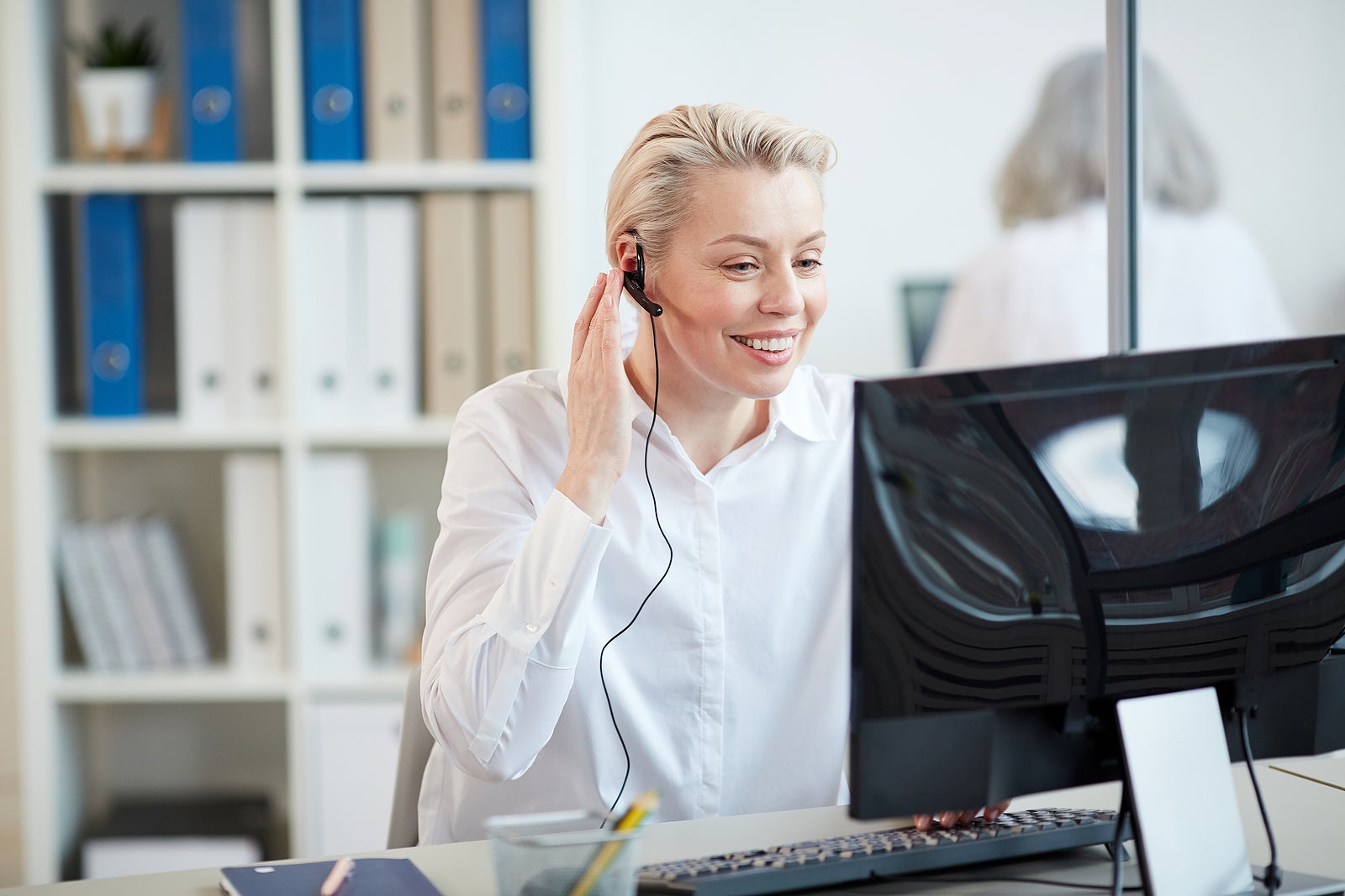 Portrait of smiling female manager wearing headset while working as customer relations operator in office interior, copy space