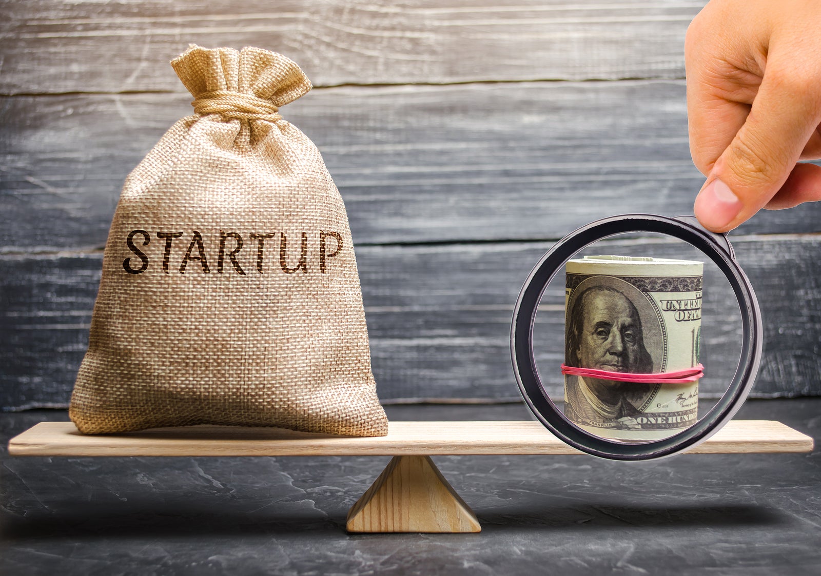 Money bag with the word Startup and dollars on the scales. Analysis of funds raised and verification of the goals of a startup. Return of money to investors after a failed startup. Achieving the fundraising goal