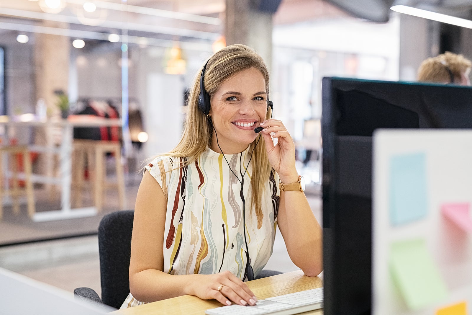 Smiling mid woman working as customer support operator with headset in a call center. Portrait of happy sales agent sitting at desk and looking at camera. Customer care support service representative.