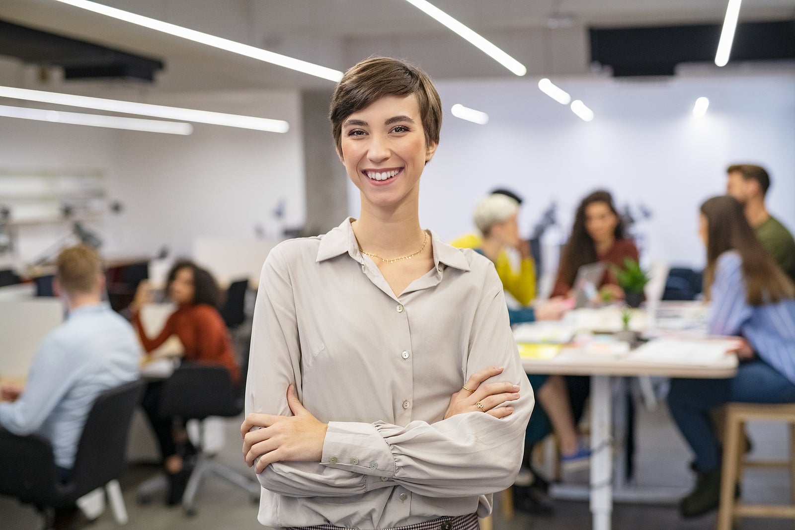 Successful young woman standing in front of businesspeople and smiling. Portrait of confident and proud businesswoman with team working in background at modern office. Business woman looking at camera