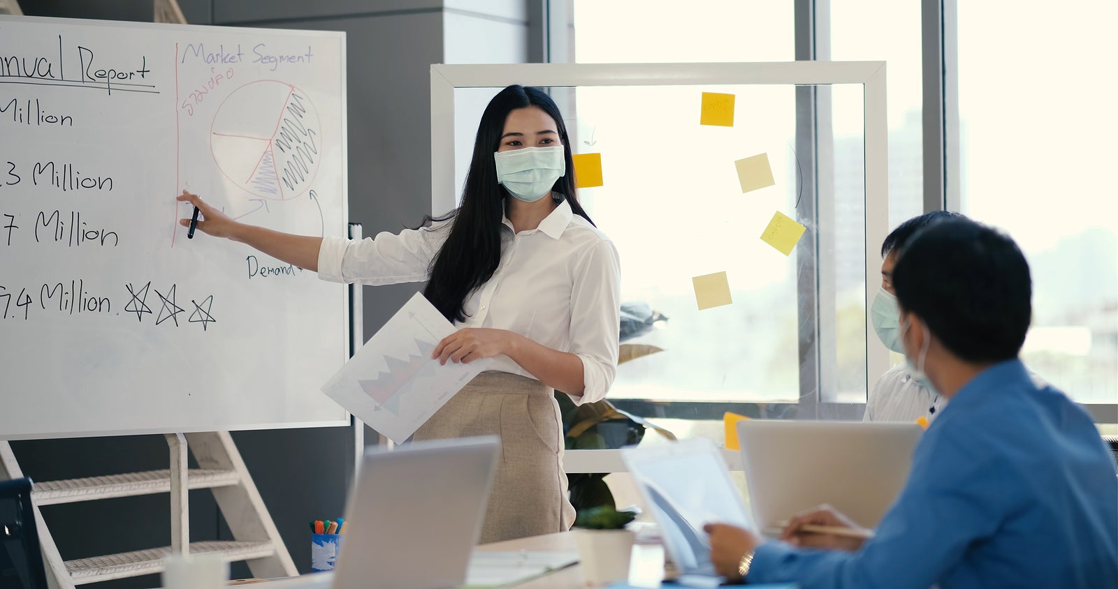 Asian business man in medical mask hand holding note paper meeting with new startup project share to business team.Group of workers sitting at table and listening speaker. Business meeting concept.