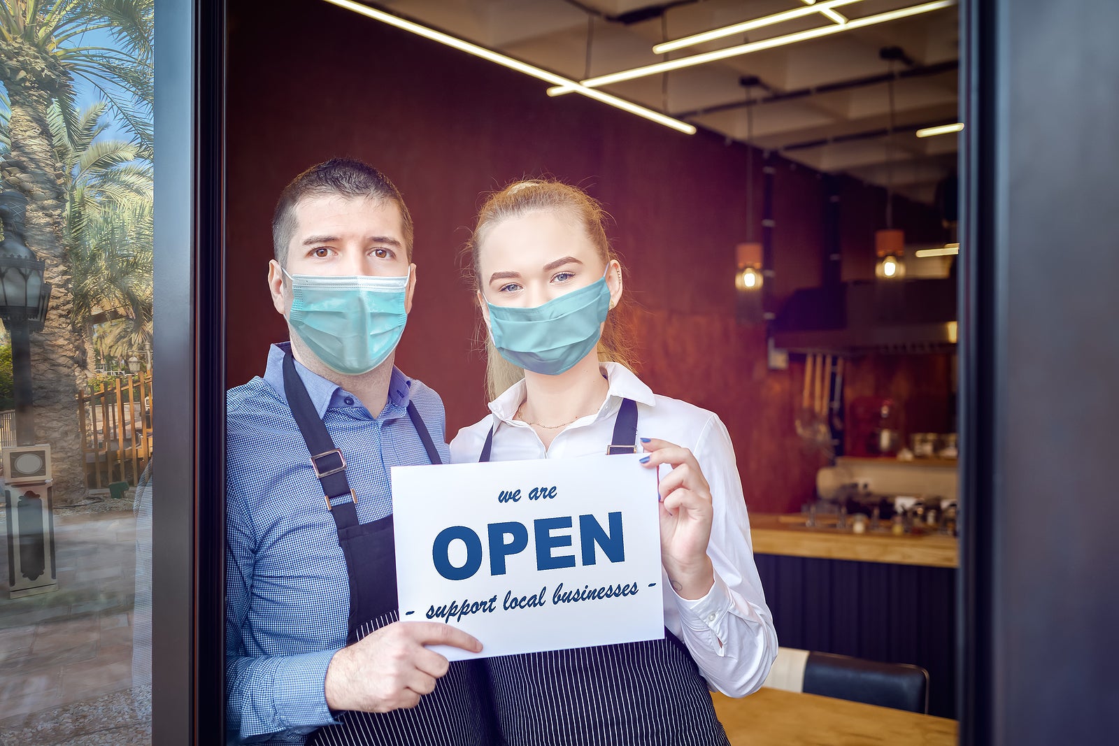 Small business owner smiling while holding sign for reopening of restaurant after lockdown quarantine due to coronavirus - Entrepeneur open coffee shop activity to support local businesses.