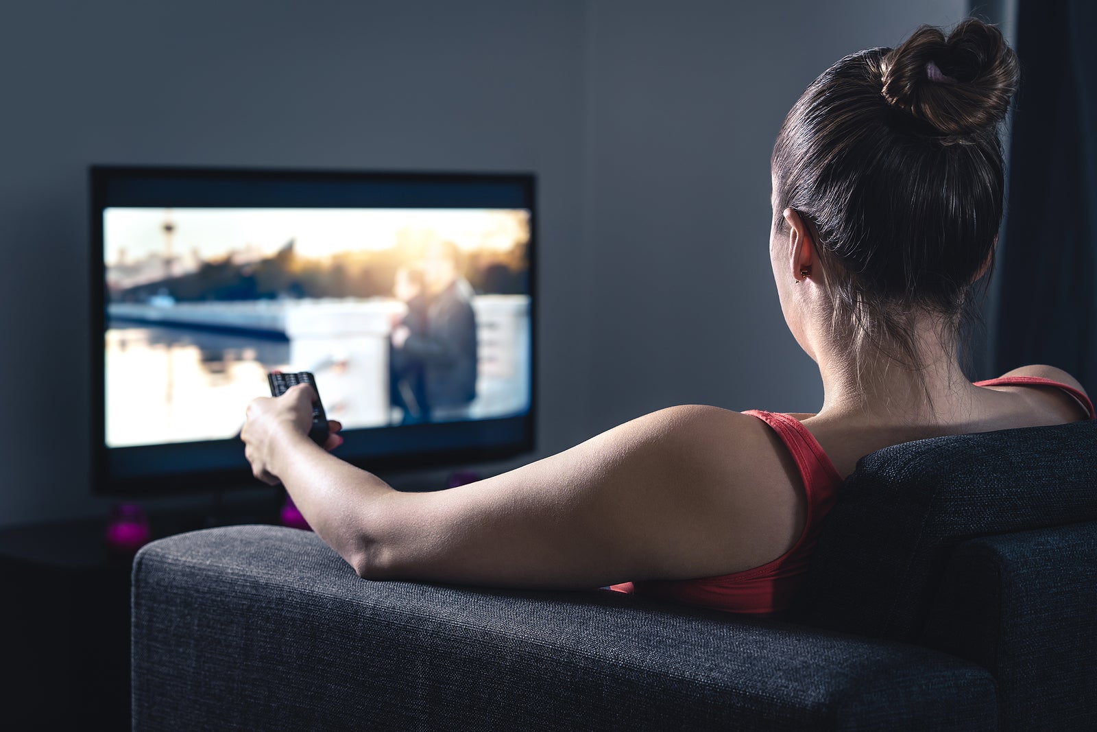 Woman streaming movie or watching series. Person using smart tv remote control to choose film or change channel. Stream or video on demand (VOD) service in television screen. Digital entertainment.