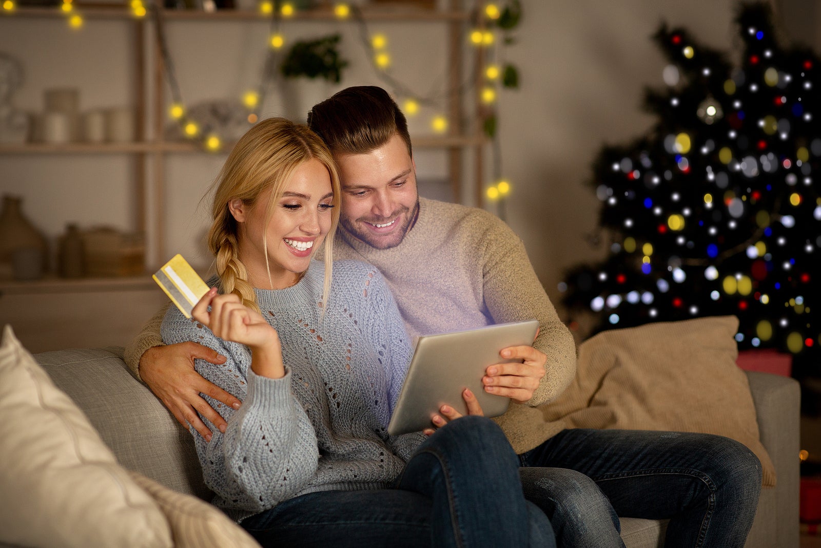 Delighted husband and wife making purchases online, using digital tablet and credit card, Christmas atmosphere at home. Happy young family shopping online on pad, using Christmas offers, copy space