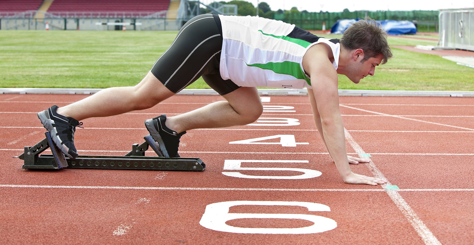 Handsome sprinter on the starting line putting his foot in the starting block in a stadium