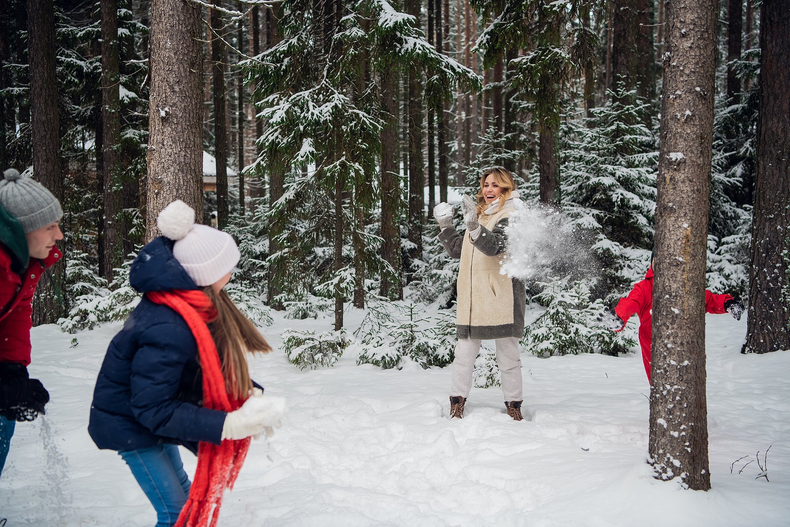 Mom, dad, son and daughter decided to play snowballs between the trees in the snow.