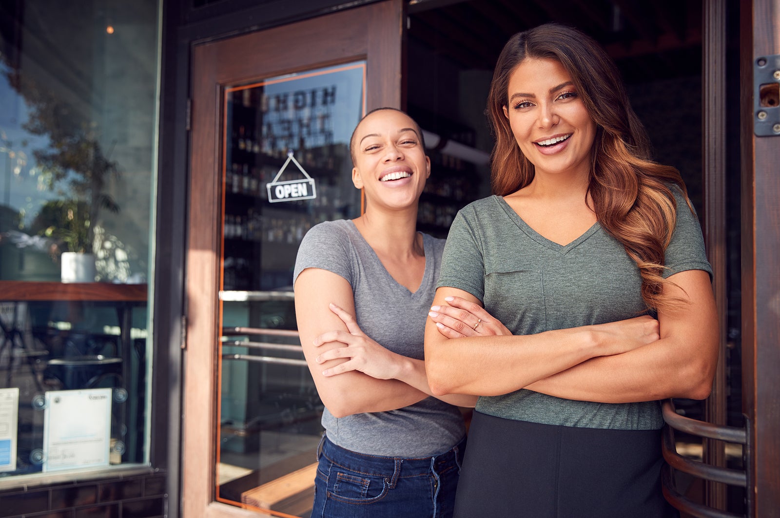 Portrait Of Two Women Starting New Coffee Shop Or Restaurant Business Standing In Doorway