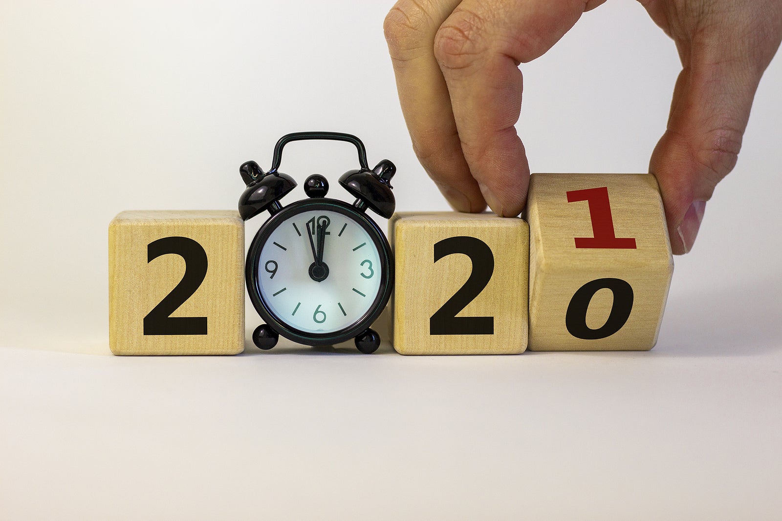 Business concept of 2021 new year. Male hand turns a wooden cube and changes number 2020 to 2021. Black alarm clock. Beautiful white background, copy space. 2021 new year concept.