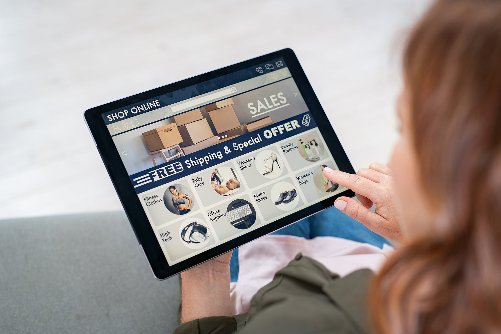 Back view of woman doing shopping online on website with digital tablet at home. Top view of lady on relaxing sofa. Rear view of girl hand touching screen while selecting product on e-commerce portal.