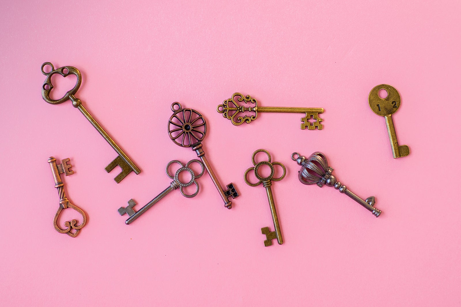 Many different old keys from different locks, scattered chaotically, flat lay. Finding the right key, encryption, concept. Retro vintage copper keys on a pink background