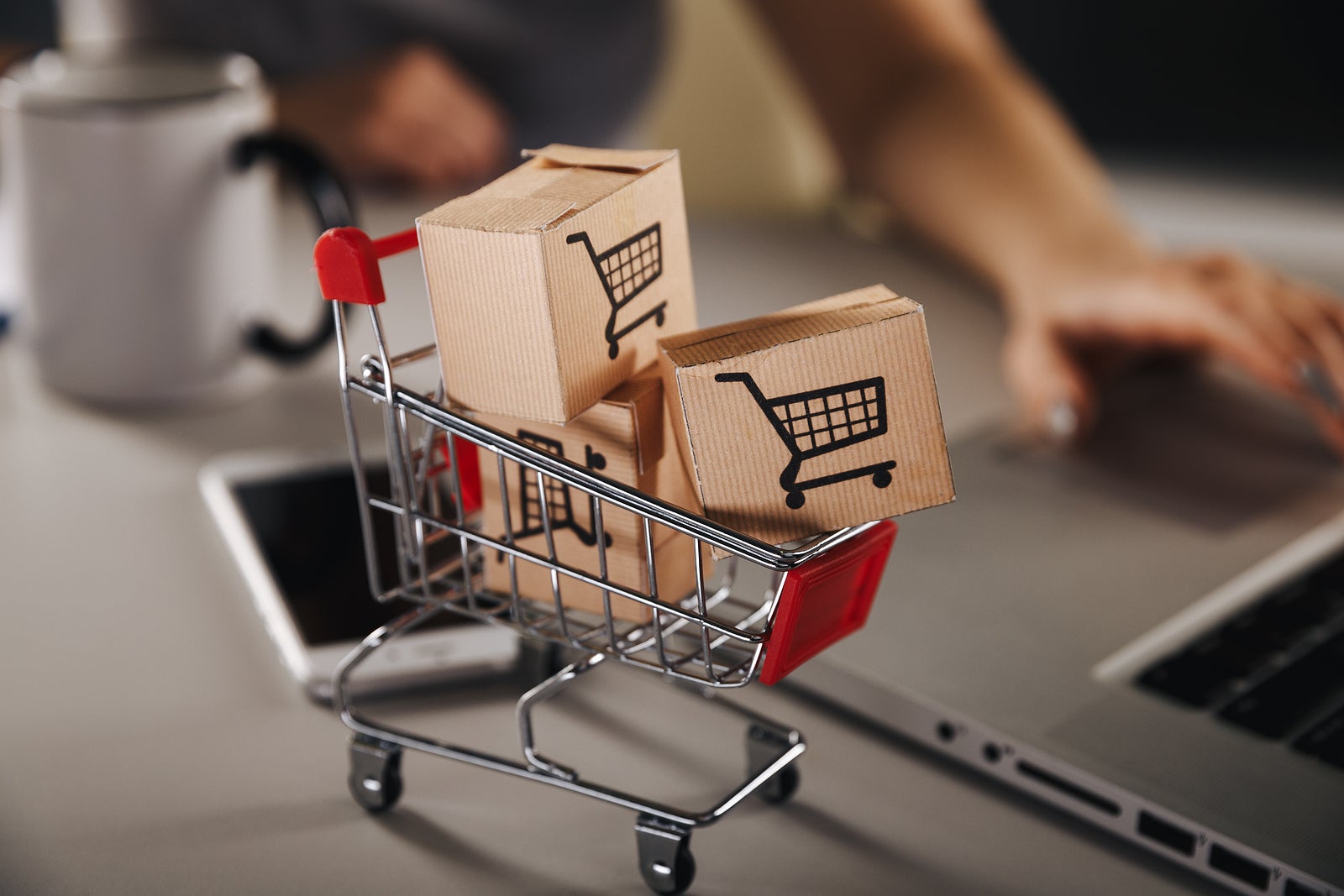 Online shopping . ecommerce and delivery service concept : Paper cartons with a cart or trolley logo on a laptop keyboard, depicts customers order things from retailer sites via the internet