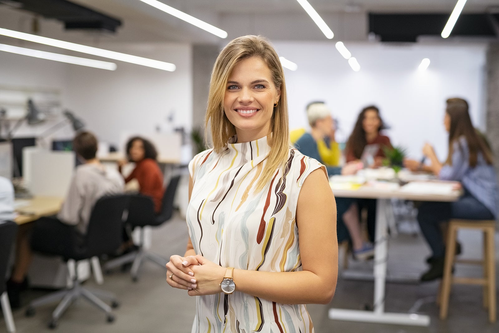 Portrait of beautiful business woman looking at camera while business team working in background. Executive woman standing in office. Happy and smiling creative businesswoman with co-workers.