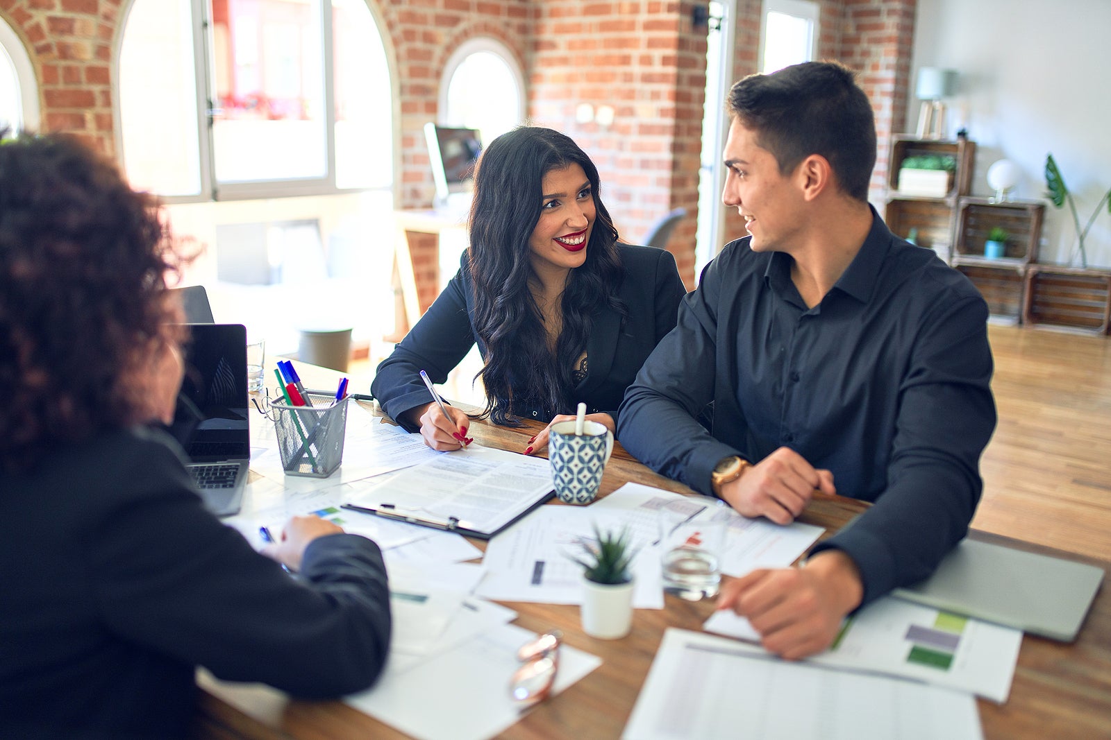 Young beautiful couple applying for mortgage. Sitting smiling happy meeting with real state agent signing mortgage loan at bank