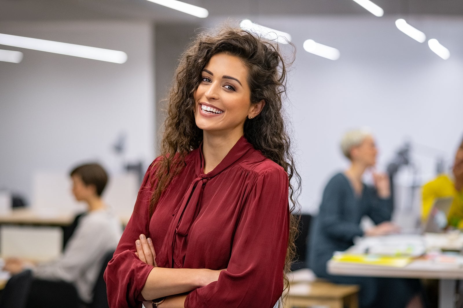 Successful businesswoman standing in creative office and looking at camera while smiling. Portrait of beautiful business woman standing in front of business team at modern agency with copy space.