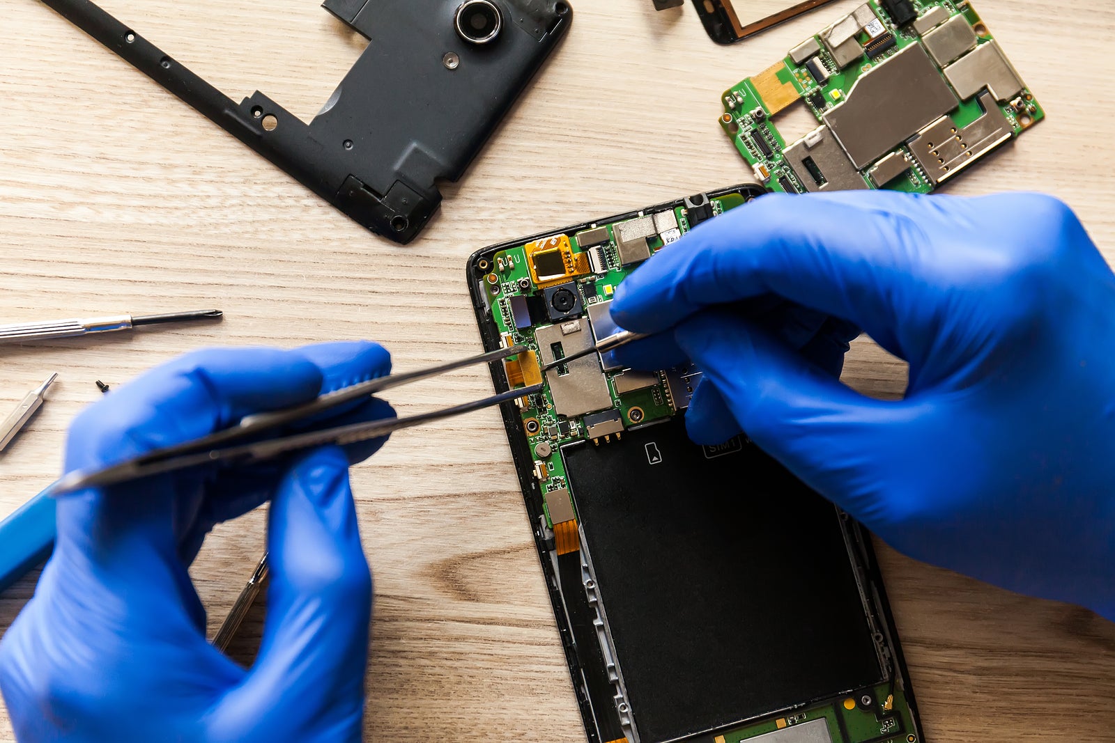 Close up of man hand repairing mobile phone with screwdriver on table. Concept of computer hardware, mobile phone, electronic, repairing, upgrade and technology.