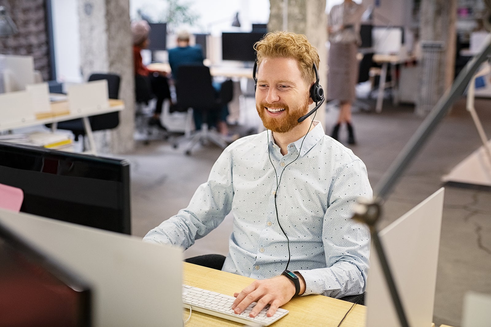 Portrait of consultant agent man in call center smiling. Happy customer support agent working with headset while sitting at his workstation. Smiling telephone operator using computer in open office.