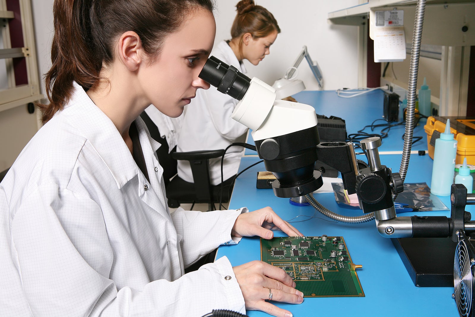 A pretty young computer technician examining a printed circuit board with a m icroscope