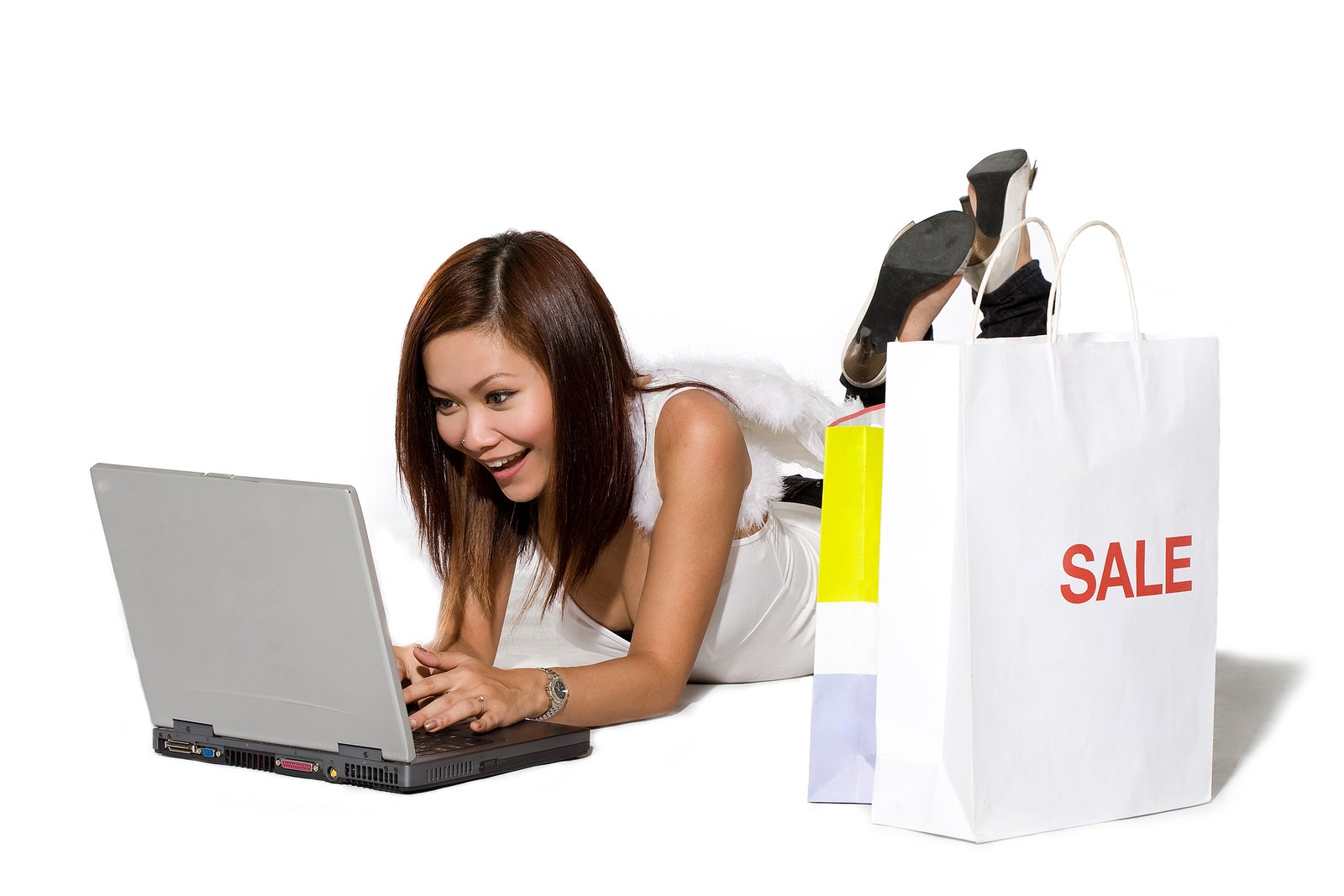 young woman happy shopping online on a laptop with paper bags by her side with angel wings