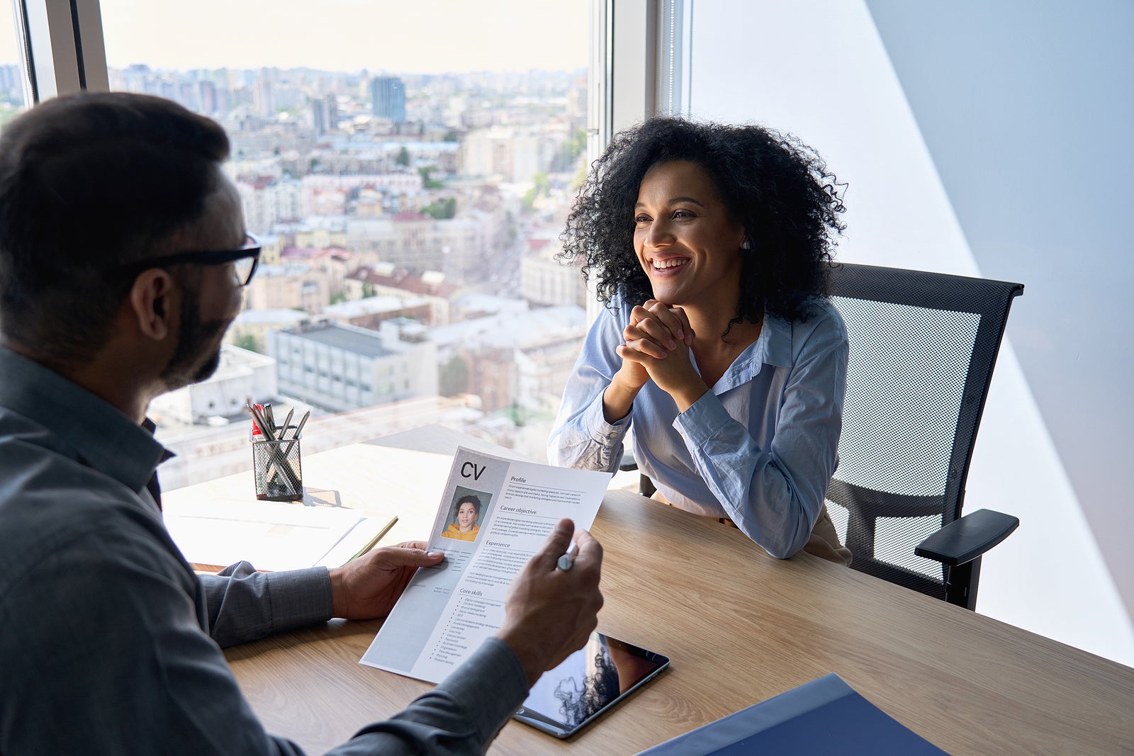 Friendly interview between Indian businessman hr director holding paper cv hiring for job female African American applicant manager sitting in contemporary office. Human resources recruitment concept.