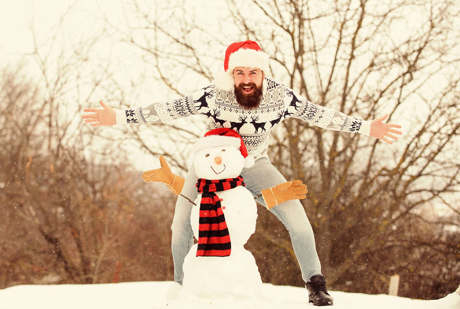 Fun and entertainment. Winter vacation. Man made snowman. Hipster with beard outdoors. Man with Santa hat having fun outdoors. Guy happy face snowy nature background. Winter games. Winter activity