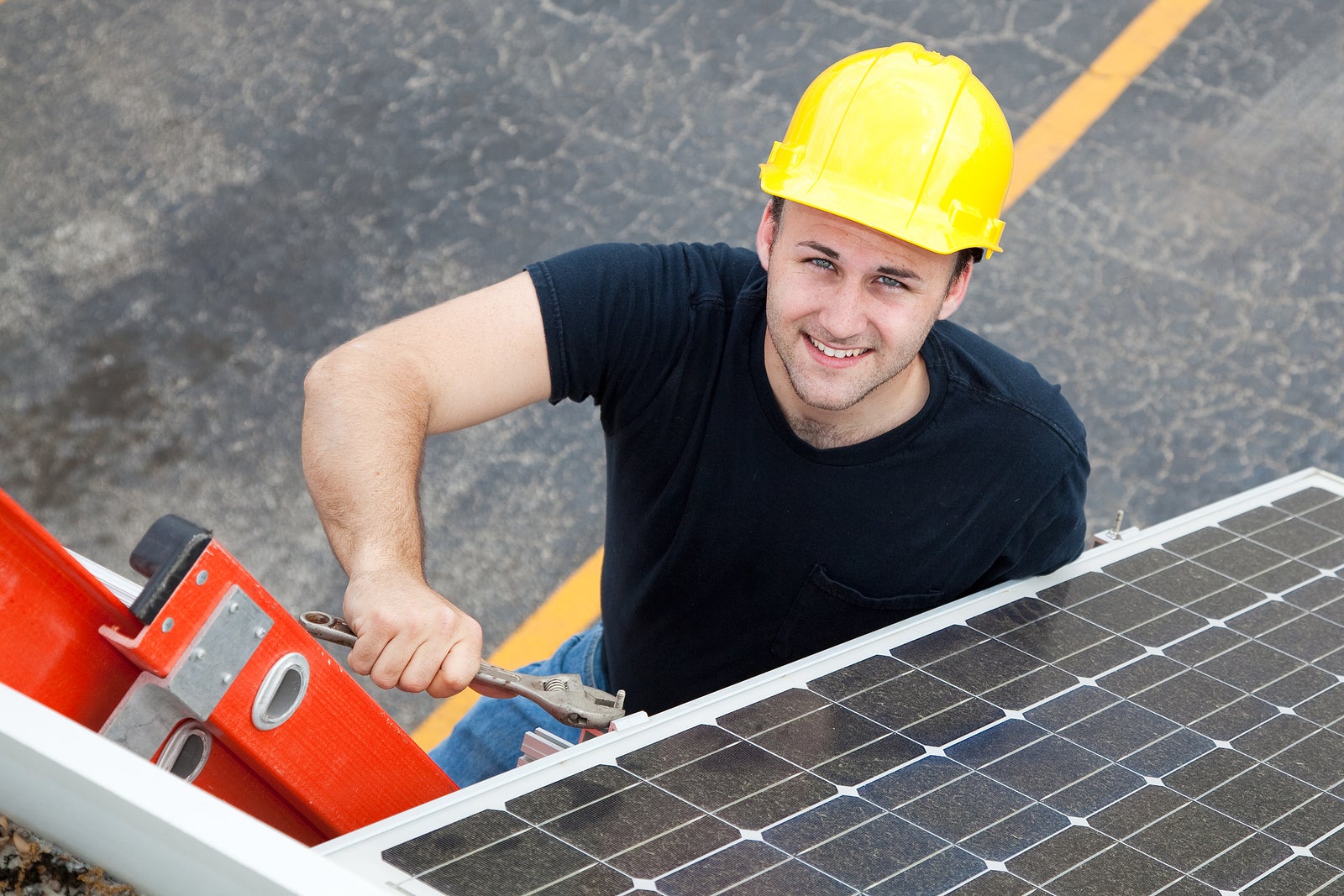 Young electrician on a ladder installing solar panels.