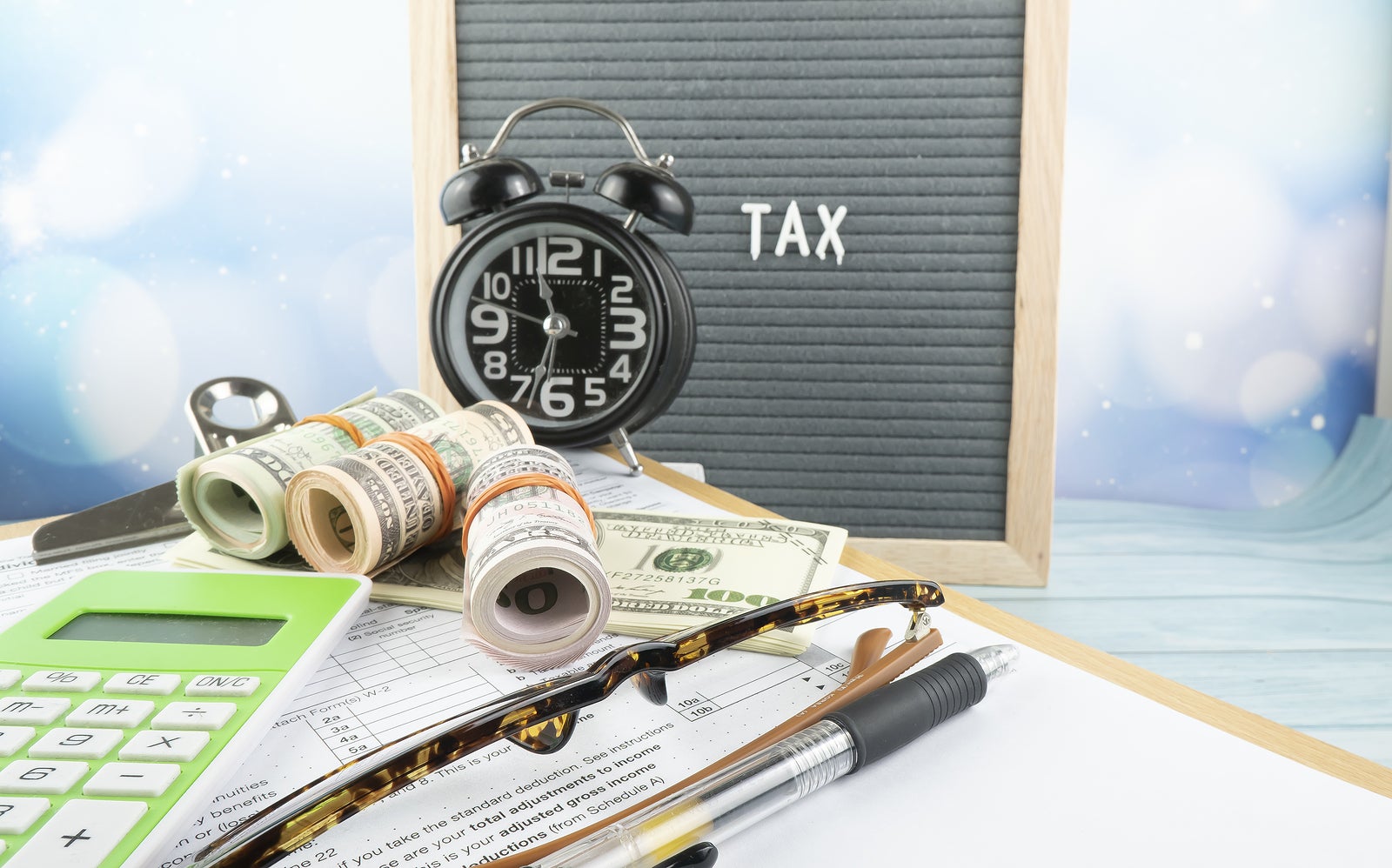 Tax-filling concept - 'Tax time' wordss. fake money, pen, eyeglasses  and a clock featuring half of U.S IRS 1040 form.