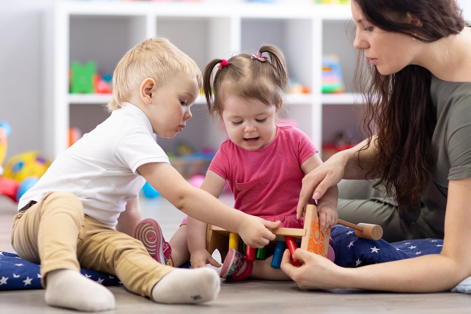 Preschooler children playing with educational wooden toys at kindergarten or daycare center. Toddlers with teacher in nursery.