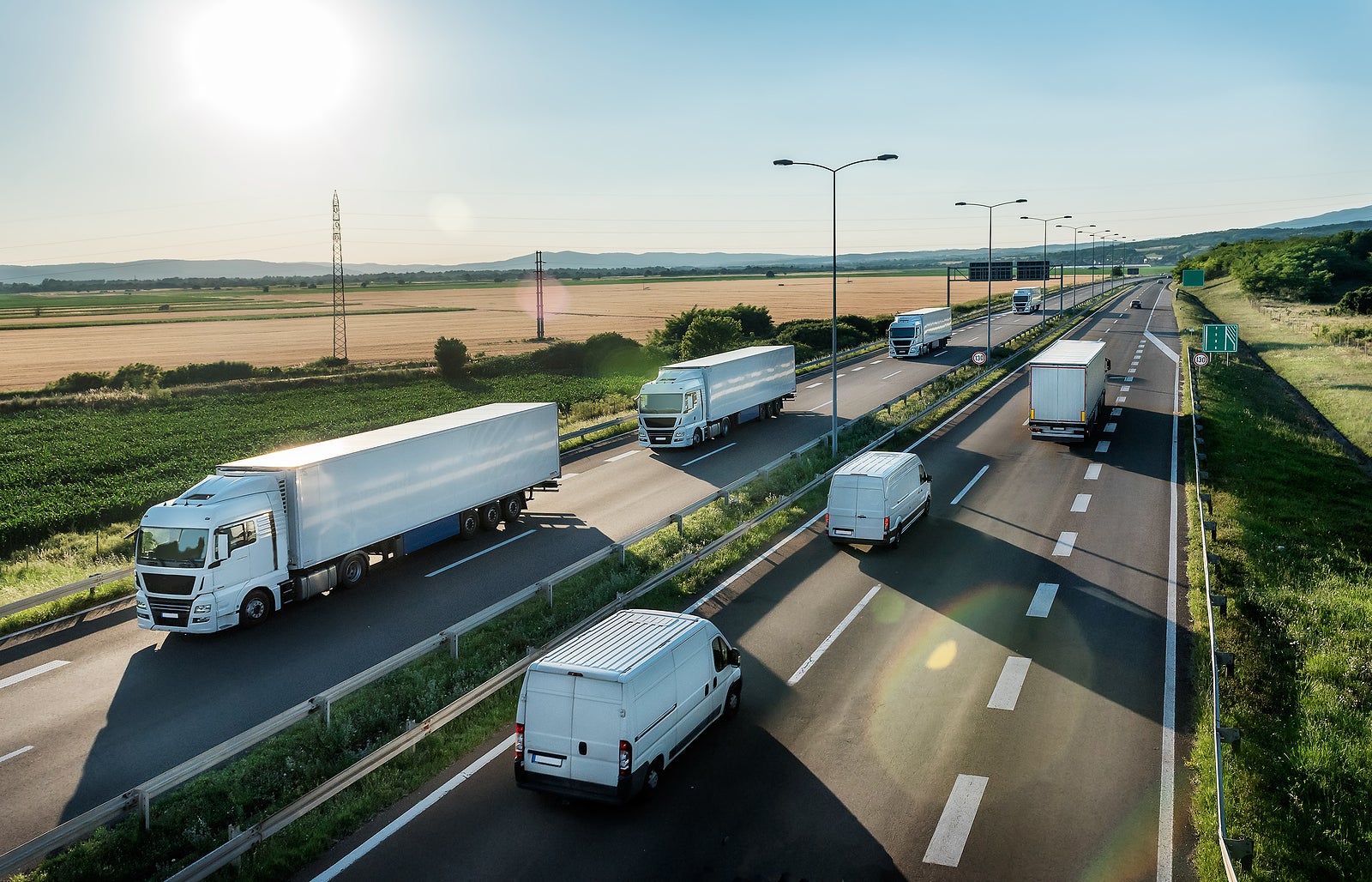 Convoy or caravans of transportation trucks passing vans and truck on a highway on a bright blue day. Highway transit transportation with lorry trucks and vans