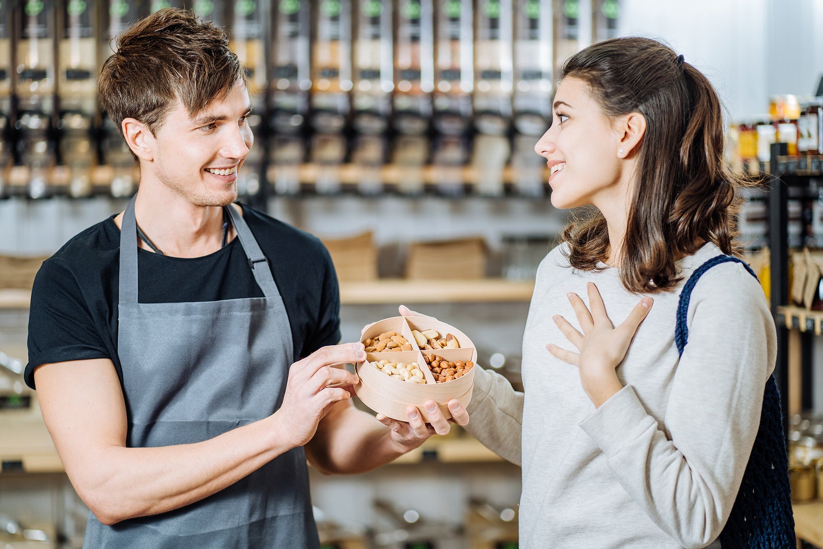 Man Owner selling nuts for brunette woman customer in Zero Waste Shop. Lots of Healthy Food in Glass Bottles on Stand in Grocery Store. No plastic Conscious Minimalism Vegan Lifestyle Concept.