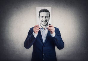 a business man hides his head behind a drawing of a smiling face